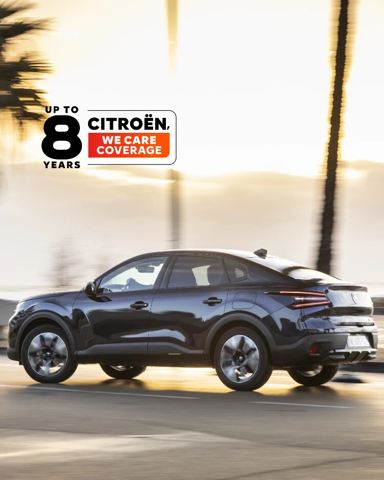 Citroën ë-C4 X fährt bei Sonnenuntergang entlang einer Küstenstraße mit dem Citroën 8-Jahres-Schutz-Abzeichen